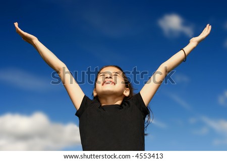 Young girl with both arms wide open, facing the bright sunshine against deep blue sky in the background, celebrating beauty of nature.
