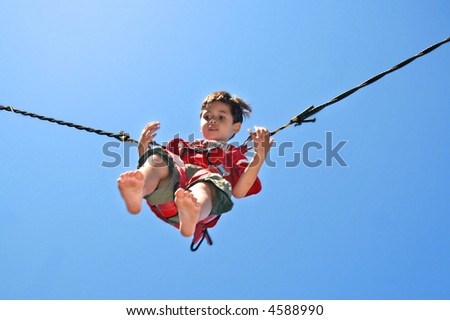 Young boy attached to jumping rope on trampoline.