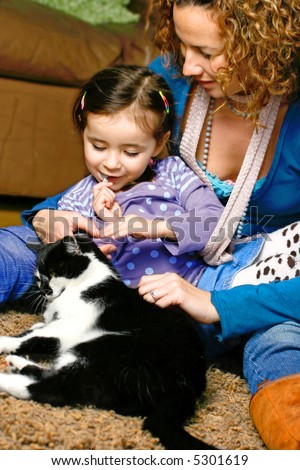 Young girl stroking the family pet cat while sitting with her mother, in a home environment
