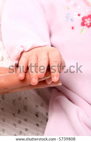 Newborn\'s hand resting at the tip of her mom\'s fingers.