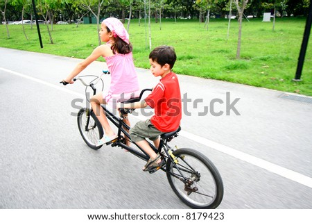 Two young children riding on a tandem bike.