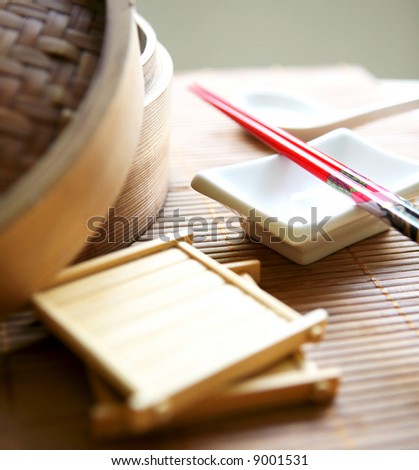 Arrangement of eating utensils ( chopsticks and spoon ) and bamboo steamers on bamboo matting.