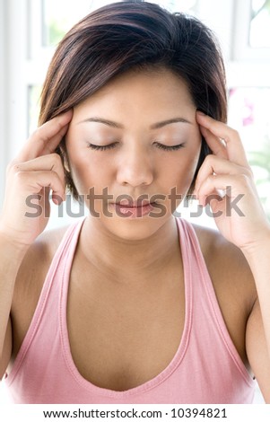Young Asian female applying gentle pressure on points on her temple to relieve headaches and tension in a calm and peaceful environment.