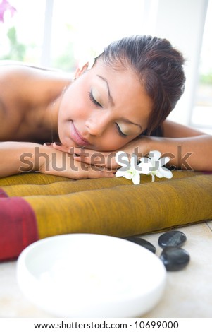 Young female on massage bed with aromatherapy bowl and therapy pebbles.