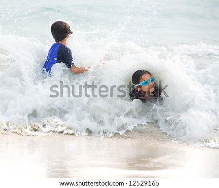 Young girl and little brother having fun being hit by a big wave at the beach.