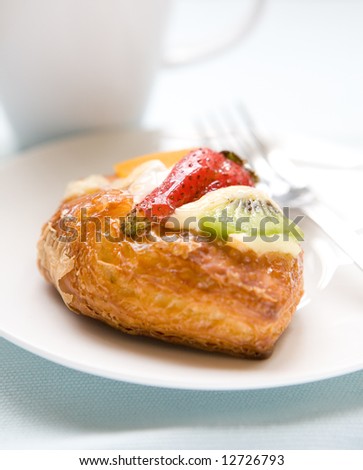 A piece of danish pastry with custard and slices of fresh fruit, kiwi, strawberry and peach.