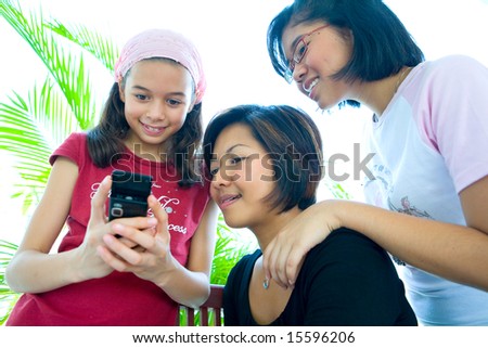 Three young girls of different ages looking at a cell phone.