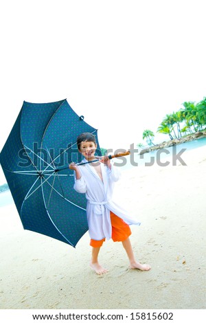 Cute little boy with a big umbrella having fun on the beach, in the rain