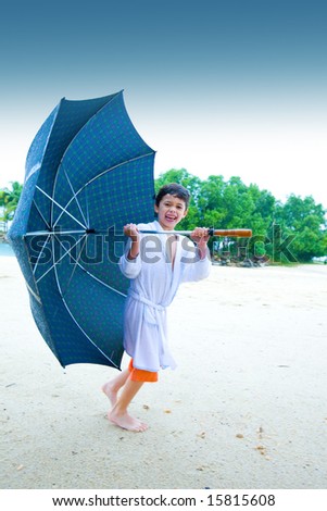 Cute little boy walking up the beach with a big umbrella in the rain