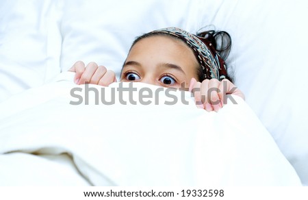 Young girl hiding behind blanket while watching scary movie