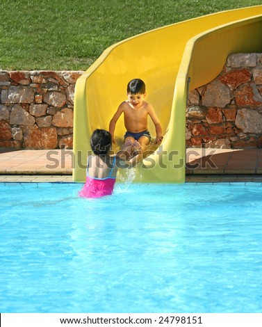Young boy getting help from his sister as he slid down the water slide at swimming pool