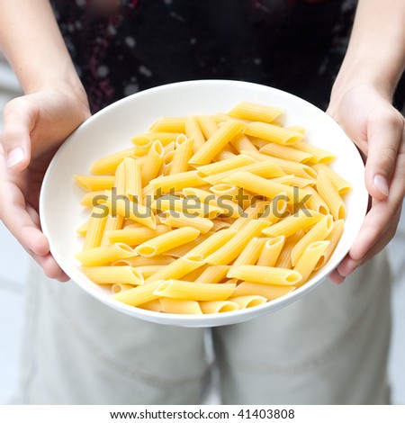Pair of hands holding a plate of dried penne pasta