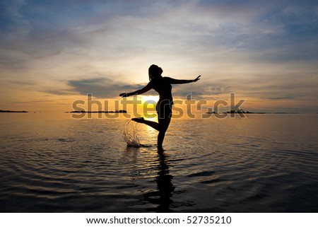 Silhouette of woman dancing in the shallow sea at sunrise