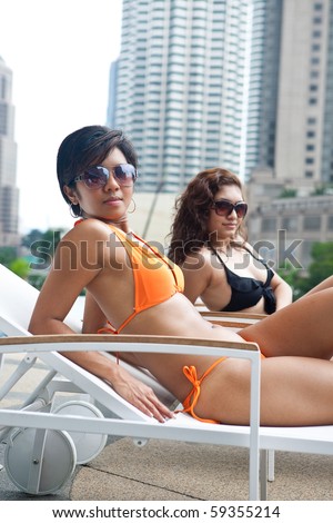 Two beautiful Asian women in bikinis resting by the pool