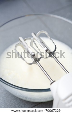 Metal egg beater with bowl of beaten eggs