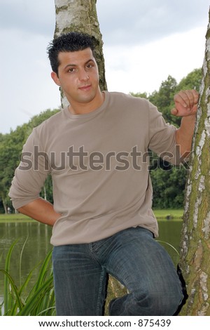 An attractive teenager on his lunch hour, taking a rest in the park. Photographed against a blue cloudy sky, leaning against a tree.
