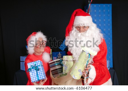 Xmas, Christmas time, santa claus and woman ready for delivering presents.  Both handing over gift towards you