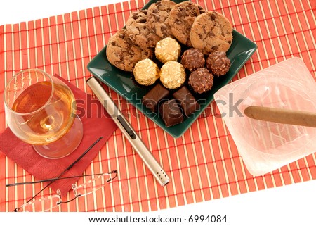 Belgium chocolates truffles, brownies on a decorative green plate. Brandy, cognac and ashtray with cigar on the side.