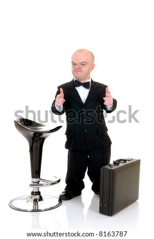 Little businessman, dwarf in a formal suit with bow tie next to bar stool and suitcase, studio shot, white background
