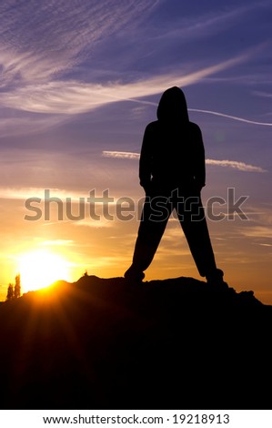 Silhouetted man with sporting outfit, sweater against sunset sky.