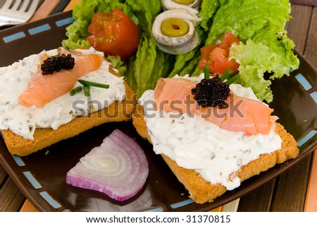 Gourmet cheese smoked salmon toast, garnished with caviar, anchovies, olives and salad.  Studio shot.