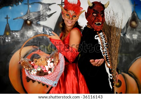 Young Halloween couple, female devil and skeleton with mask, basket with sweets.    Studio shot, graffiti  background.