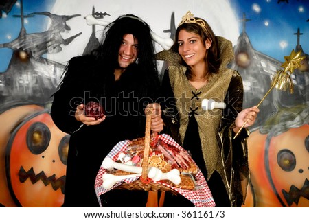 Young Halloween couple, female witch and man with sinister costume, basket with sweets.    Studio shot, graffiti  background.