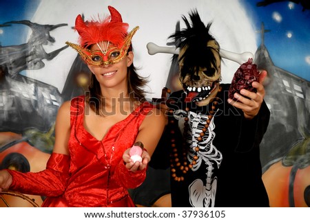 Young Halloween couple, female devil and skeleton with mask, basket with sweets.    Studio shot, graffiti  background.