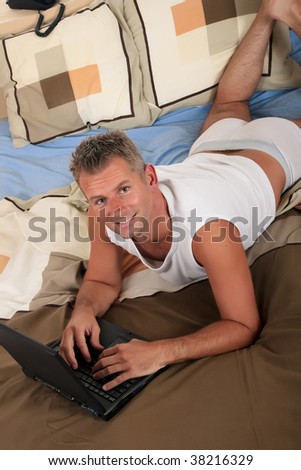 Handsome forties man surfing on internet with laptop on bed in bedroom.  Studio.