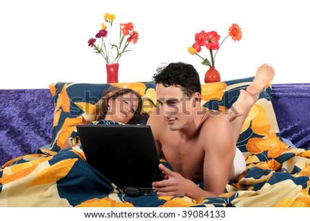 young loving couple grooming in bed, man surfing on internet with laptop, woman sleeping.  Studio.