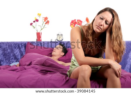 young  couple on bed in bedroom, woman having a depression moment while husband sleeping.  Studio.