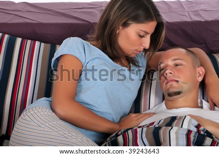 Young handsome man sick in  bed, thermometer in mouth.  Women nursing husband. Studio.