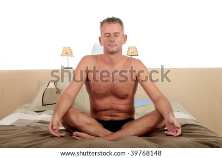 Handsome forties man  grooming on bed in bedroom, yoga position.  Studio.