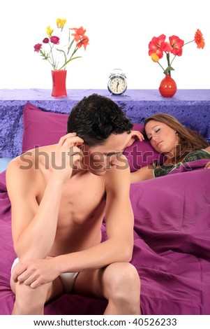 young  couple on bed in bedroom, man having a depression moment while wife is sleeping.  Studio.