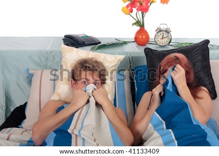 young loving couple, in bed in bedroom, hiding behind sheets, watching horror movie on television.  Studio.