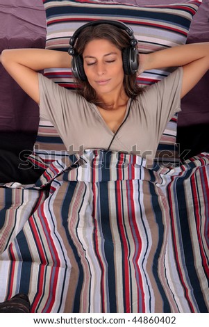 young attractive woman on bed in bedroom,  listening music with headset.  Studio.