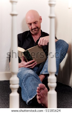 Bald Middle aged man reading book sitting on floor, artistic composition, shallow dof, focus on man.