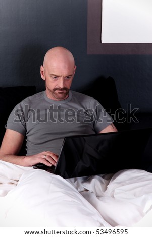 Bald Middle aged man working on laptop on bed in bedroom.