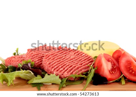 Raw hamburgers, tomatoes and peeled potato on cutting board.  Studio, white background. Shallow dept of field, focus on front hamburger.