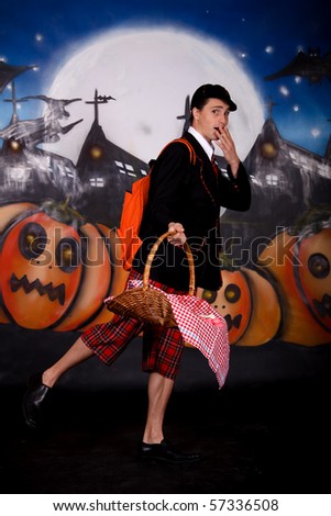 Young Halloween male with English boarding school student outfit holding basket with sweets.    Studio shot, painted background.