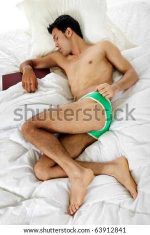 Young handsome Nepalese man on the bed, sleeping after reading a book. Studio shot. White background.