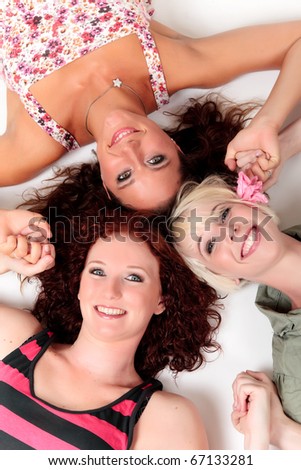 Three young attractive women lying on the floor holding the hands. Studio shot. White background