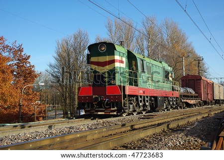 The locomotive pulls  wagons, around autumn park; suburb.
