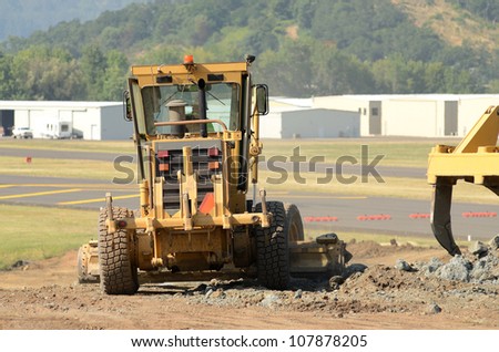 Road grader smoothing the road at a large construction site removing a hill during an airport runway expansion project