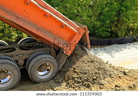 A 10 yard dump truck dumps its load of rock and soil on a new road construction project