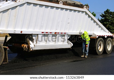 A large belly dump truck delivers fresh asphalt for a paving project of a new road and intersection project