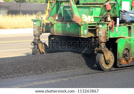 Asphalt paving machine laying down a fresh layer of paving on a new road interchange project