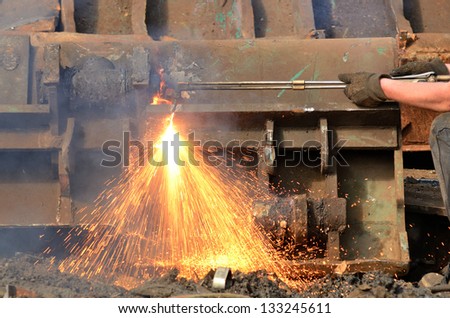 A worker uses a oxygen acetylene cutting torch to cut a large metal object into manageable pieces at a metal recycling plant