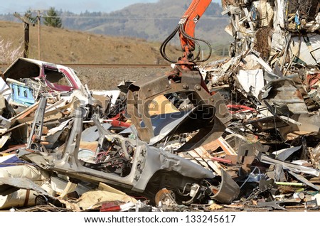 Boom mounted claw breaking up a small car at a metal recycling plant before crushing,