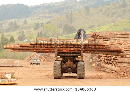 A large wheeled front end log loader working the log yard at a lumber processing mill that specializes in small logs